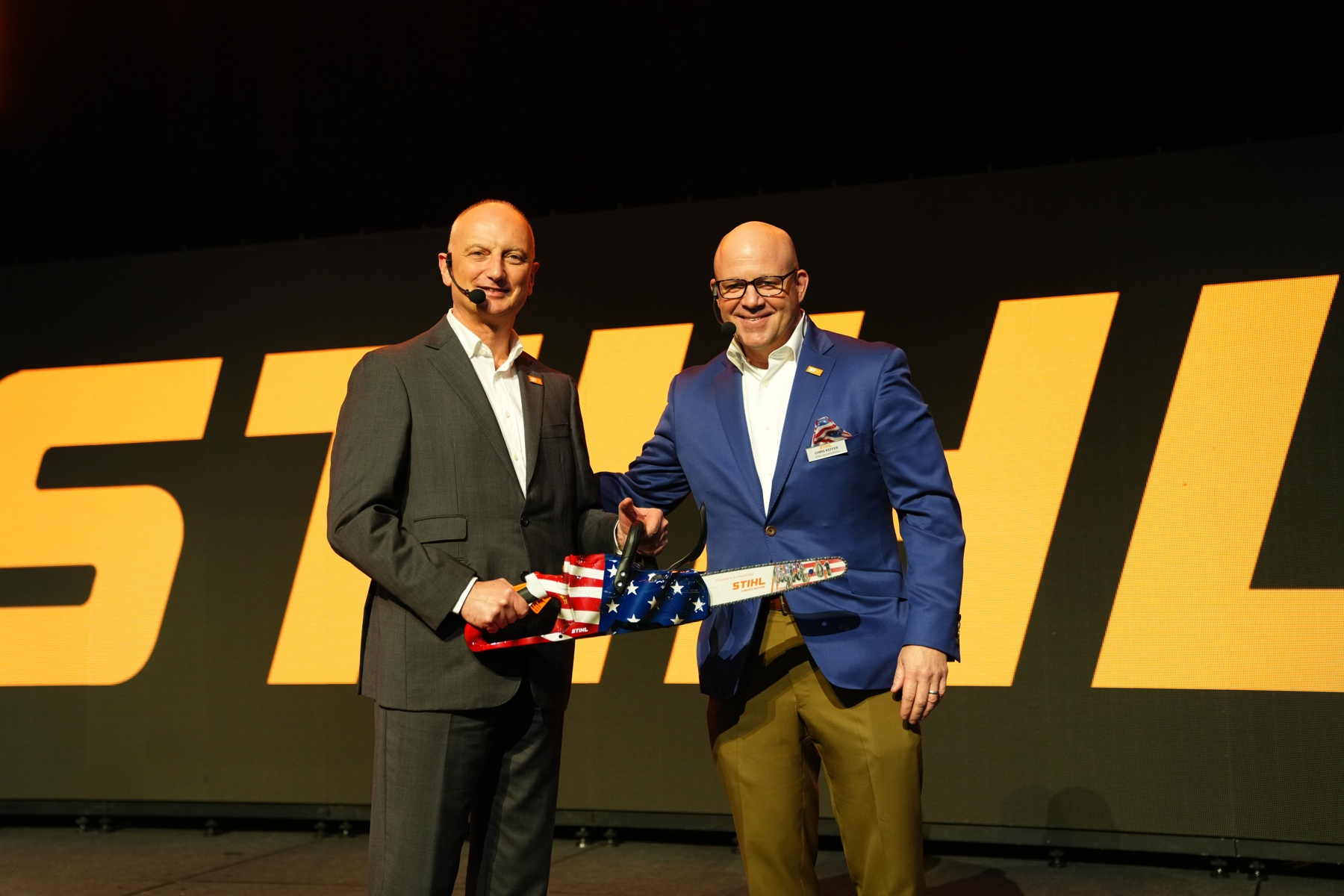 Dr. Nikolas Stihl (stânga) și Chris Keffer, director general al STIHL Inc. în SUA, prezintă un ferăstrău aniversar cu un steag american.